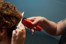 Red cordless hair clipper cutting the side of curly hair