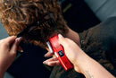 Red cordless hair clipper trimming curly hair with an open blade