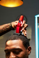 Red cordless hair clipper held near the top of a closely shaved head
