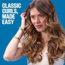 Curling attachment in teal-and-black held near long hair for loose curls