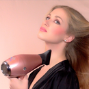 Rose gold hair dryer held near a person’s shoulder, black nozzle facing left