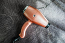 Rose gold hair dryer lying on a surface with black nozzle and cord