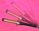 Gold-barrel curling iron with black control handle and hinged clamp, shown with cover cap