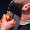 Handheld orange cordless clipper trimming dark hair near the ear