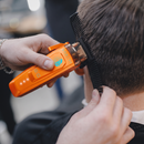 Orange cordless hair clipper in use, trimming hair with guard comb