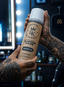 Unscented clipper care spray can held in a hand with visible tattooed forearm