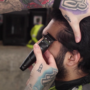 Black handheld electric hair trimmer being used near the hairline; metal head visible.