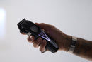 Black cordless hair clipper with blue-lit button on handle, blade facing up
