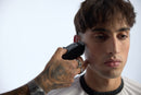 Black cordless hair clipper held to man’s cheek, blue light visible on handle