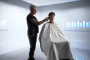Barber using black cordless hair clipper while client wears a cape