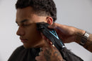 Black cordless hair clipper cutting hair along the side, blue indicator light