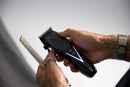 Black cordless hair clipper held with comb attachment visible near blade